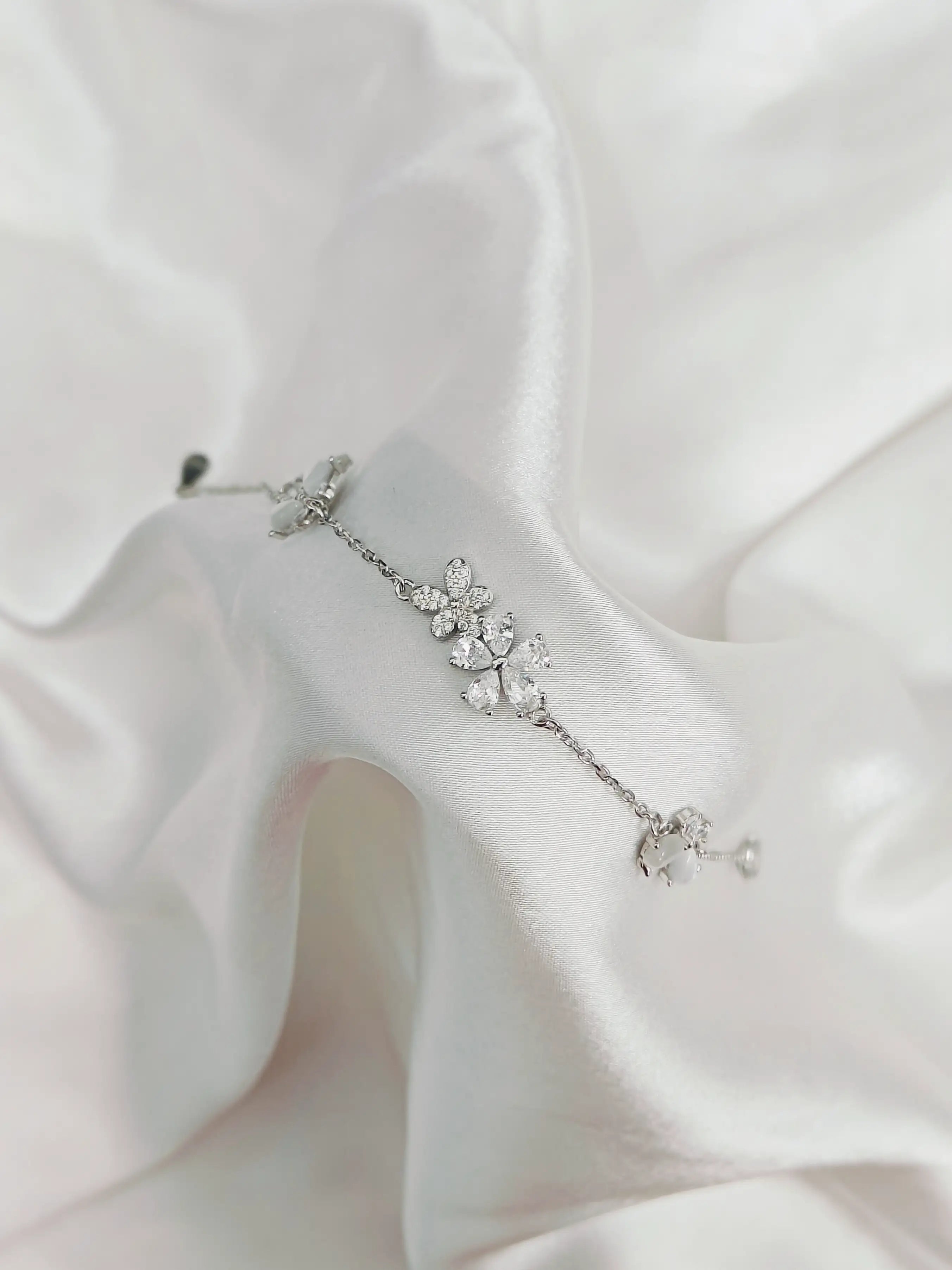 Silver floral earring on a white fabric background